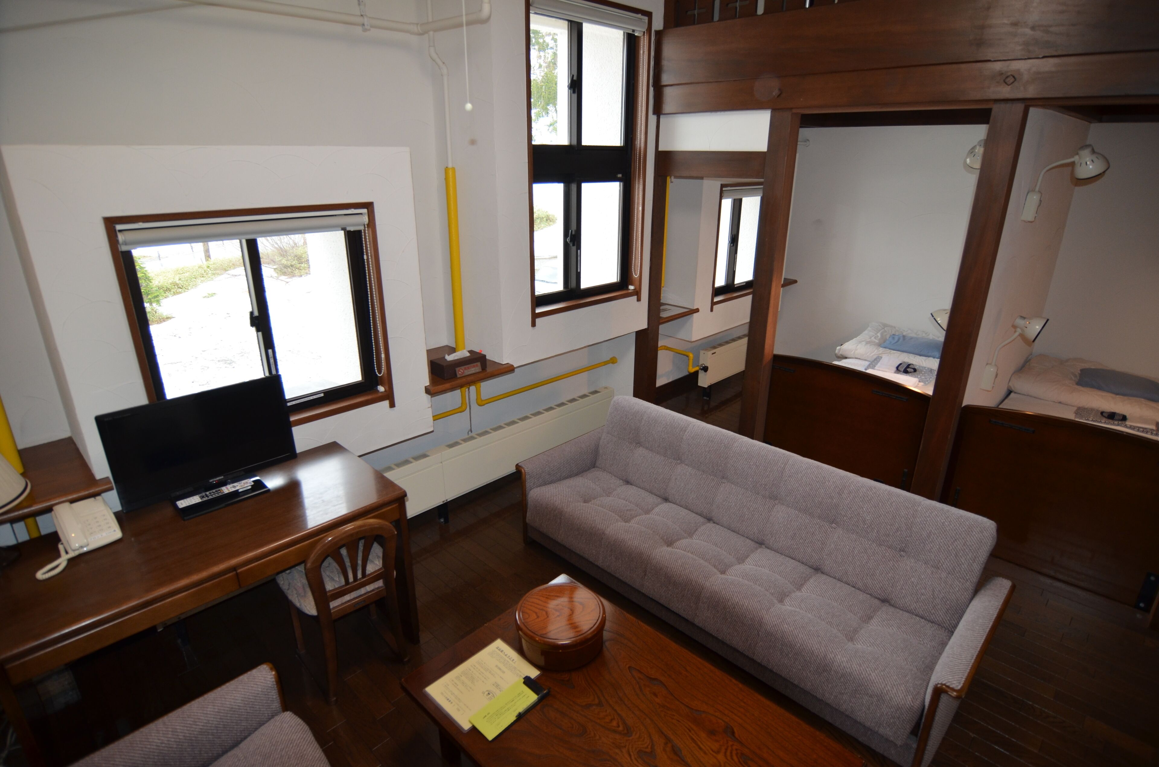 Ein Zimmer mit einer Couch, einem Schreibtisch mit Computer, einem Telefon und einem Fenster mit Jalousien.