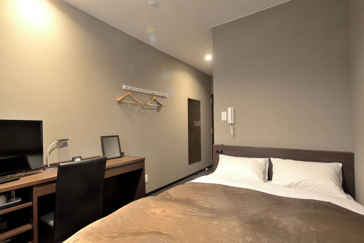 A hotel room with a bed, desk, chair, television, and a wall-mounted towel rack.