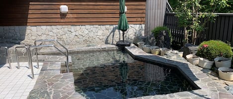 Un jacuzzi con suelo de piedra, una terraza de madera y un paraguas verde.