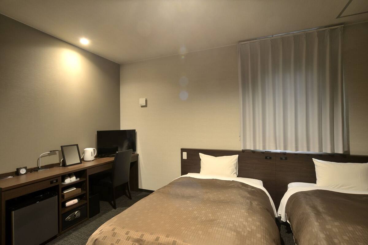 A hotel room with a bed, a desk, a television, a coffee maker, and a window with curtains.