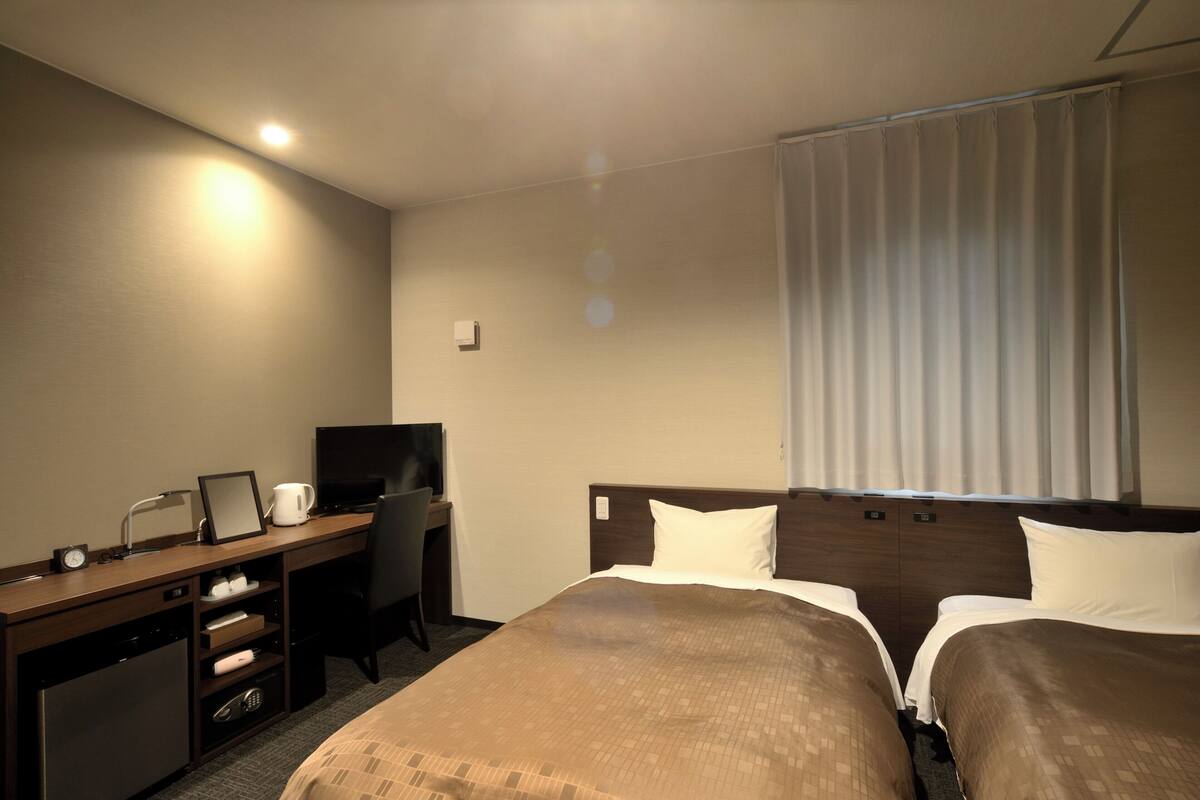 A hotel room with a bed, a desk with a computer, a television, and a small kitchenette.