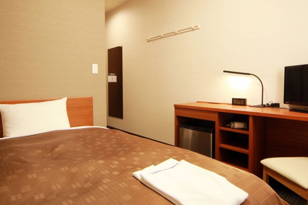 Una habitación de hotel con una cama, un escritorio con una computadora, un televisor y un mueble pequeño.