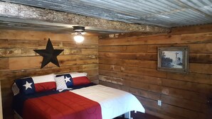 Une pièce aux murs en bois, un lit recouvert d’une courtepointe ornée du drapeau du Texas, une décoration en forme d’étoile et un tableau encadré accroché au mur.