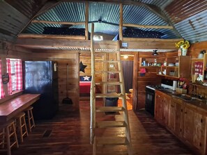 Cocina rústica con pisos de madera, una escalera de madera en el centro y un techo de lámina corrugada a gran altura.