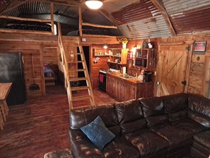 Interior acogedor de una cabaña con una mesa de comedor de madera, un sofá de cuero, una zona de cocina y una escalera que lleva a un nivel superior.