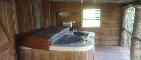 Una cabaña de madera con un jacuzzi, una ventana y una terraza de madera.