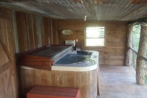 A wooden cabin with a hot tub, a window, and a wooden deck.