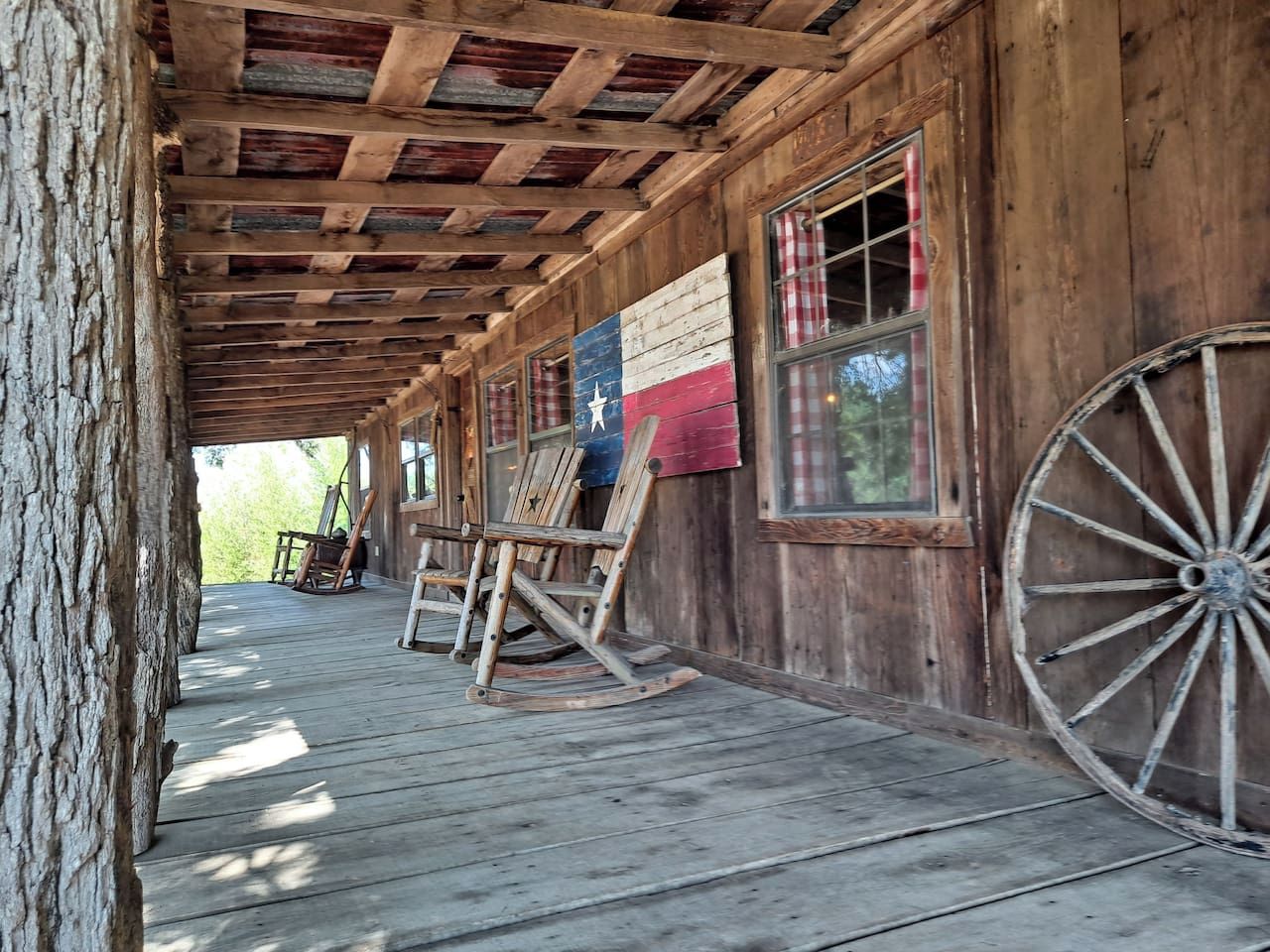 A wooden porch with rocking chairs, a flag, and a large wheel.