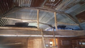 Un intérieur rustique en bois, avec un toit en tôle ondulée, une échelle en bois et un lit avec un oreiller.