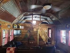 L’intérieur d’un chalet rustique, avec un escalier en bois, un téléviseur, un sapin de Noël et un canapé en cuir.