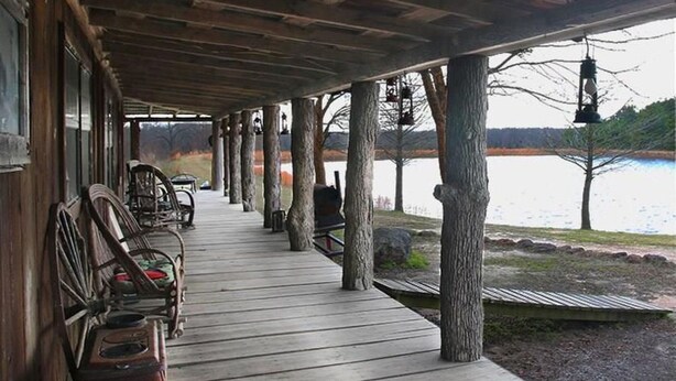 Une terrasse en bois couverte, dotée de bancs et offrant une vue sur un lac.