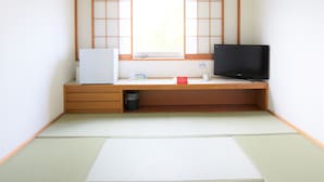 Een minimalistische kamer in Japanse stijl met tatami vloeren, een laag houten bureau, een witte koelkast, een flatscreen televisie en een raam met uitzicht.