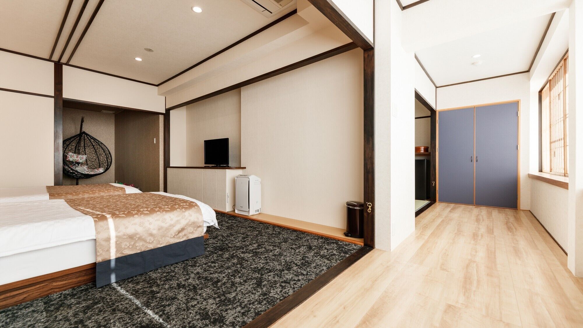A modern hotel room with a large bed, a hanging chair, a television, and a wardrobe.