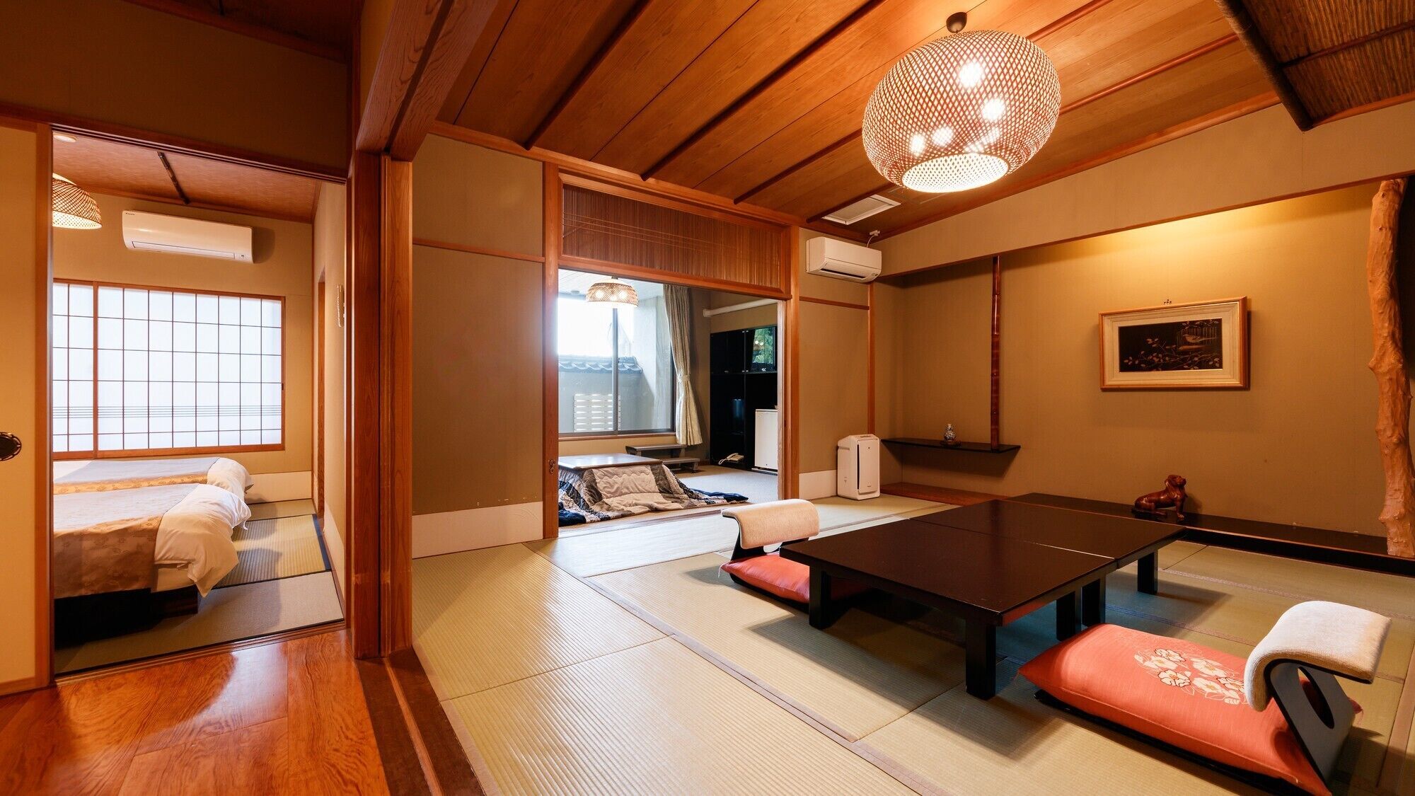 Una habitación japonesa tradicional con suelo de tatami, una mesa baja, cojines e una lámpara colgante.