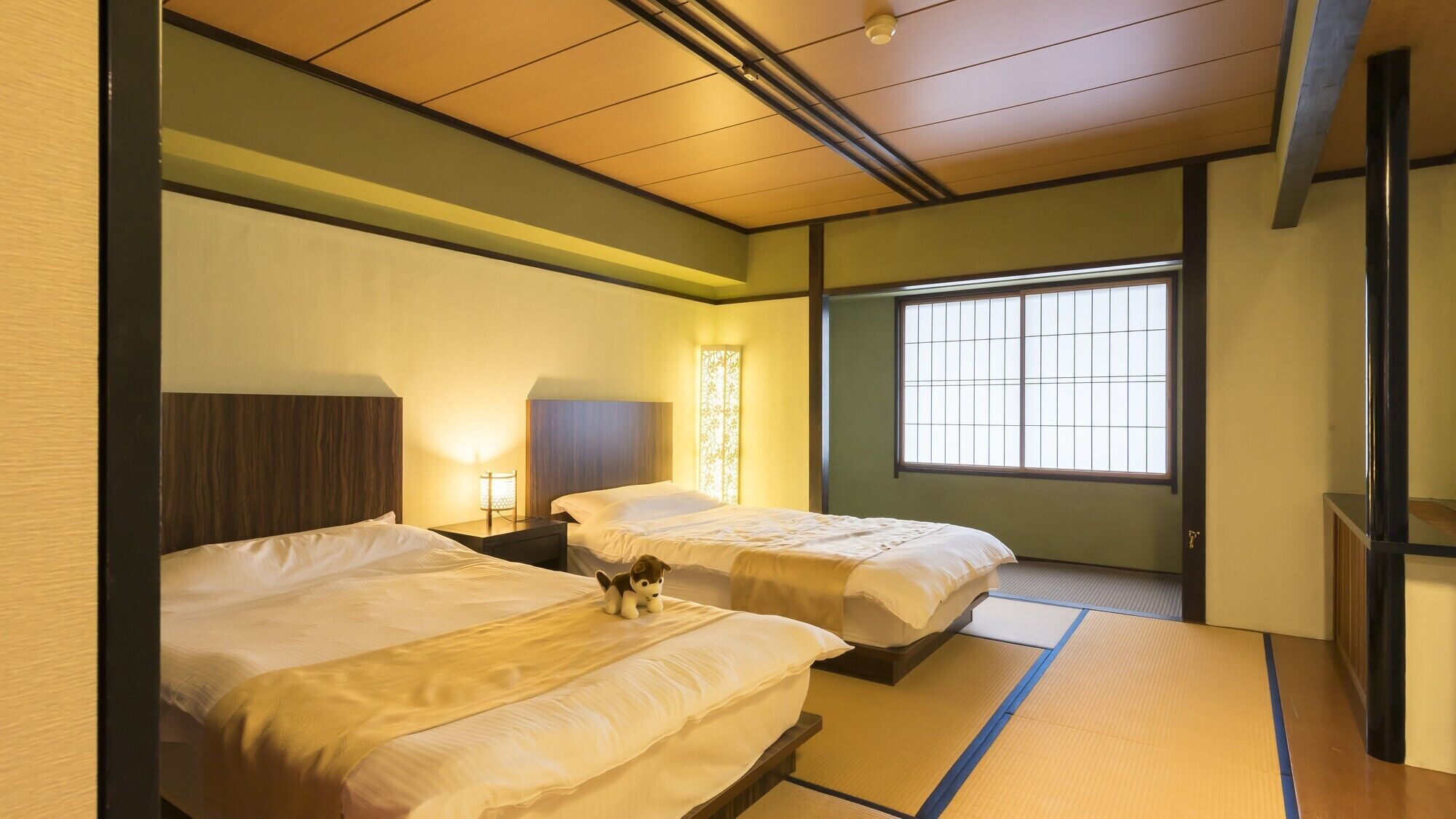 A hotel room with two beds, a window with a view, and a traditional Japanese-style floor mat.