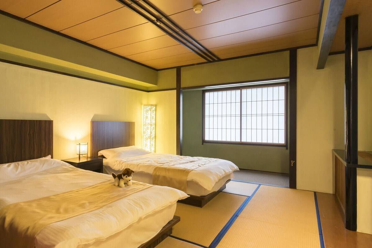 Una habitación de hotel con dos camas, una ventana con vistas y un tapete de suelo tradicional japonés.