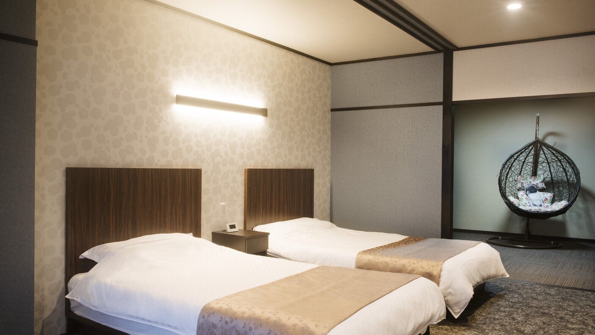 A hotel room with two beds, a hanging chair, and a wall-mounted light.