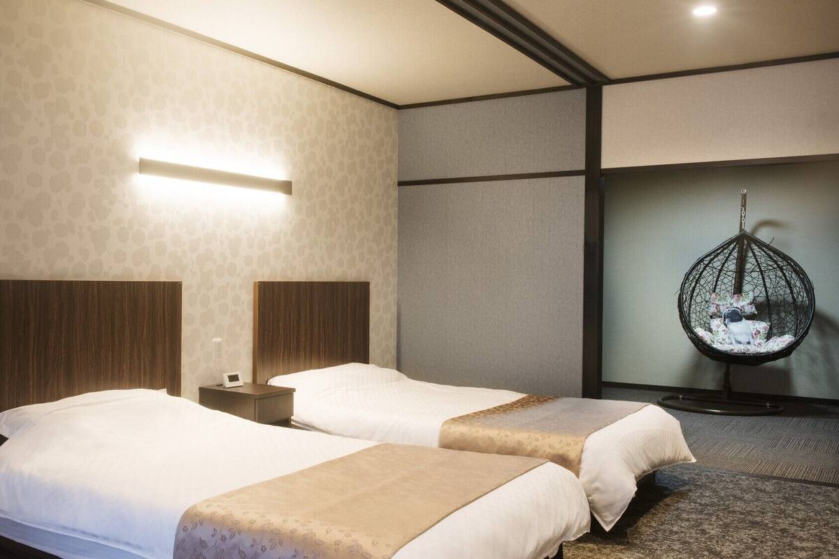 Una habitación de hotel con dos camas, un sillón colgante y una lámpara de pared.