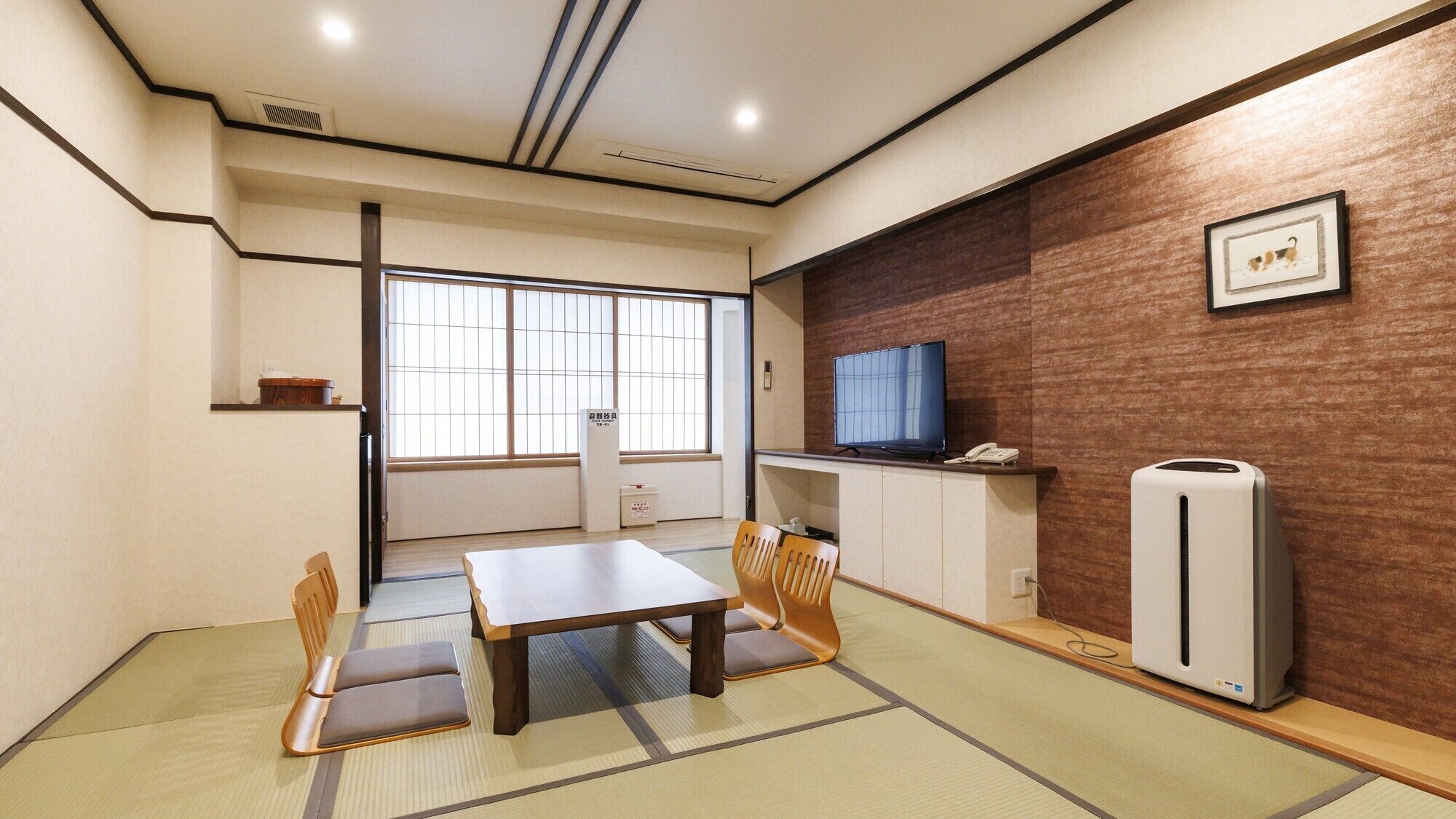 A room with tatami flooring, a low table, chairs, a television, a refrigerator, and a window with a view.