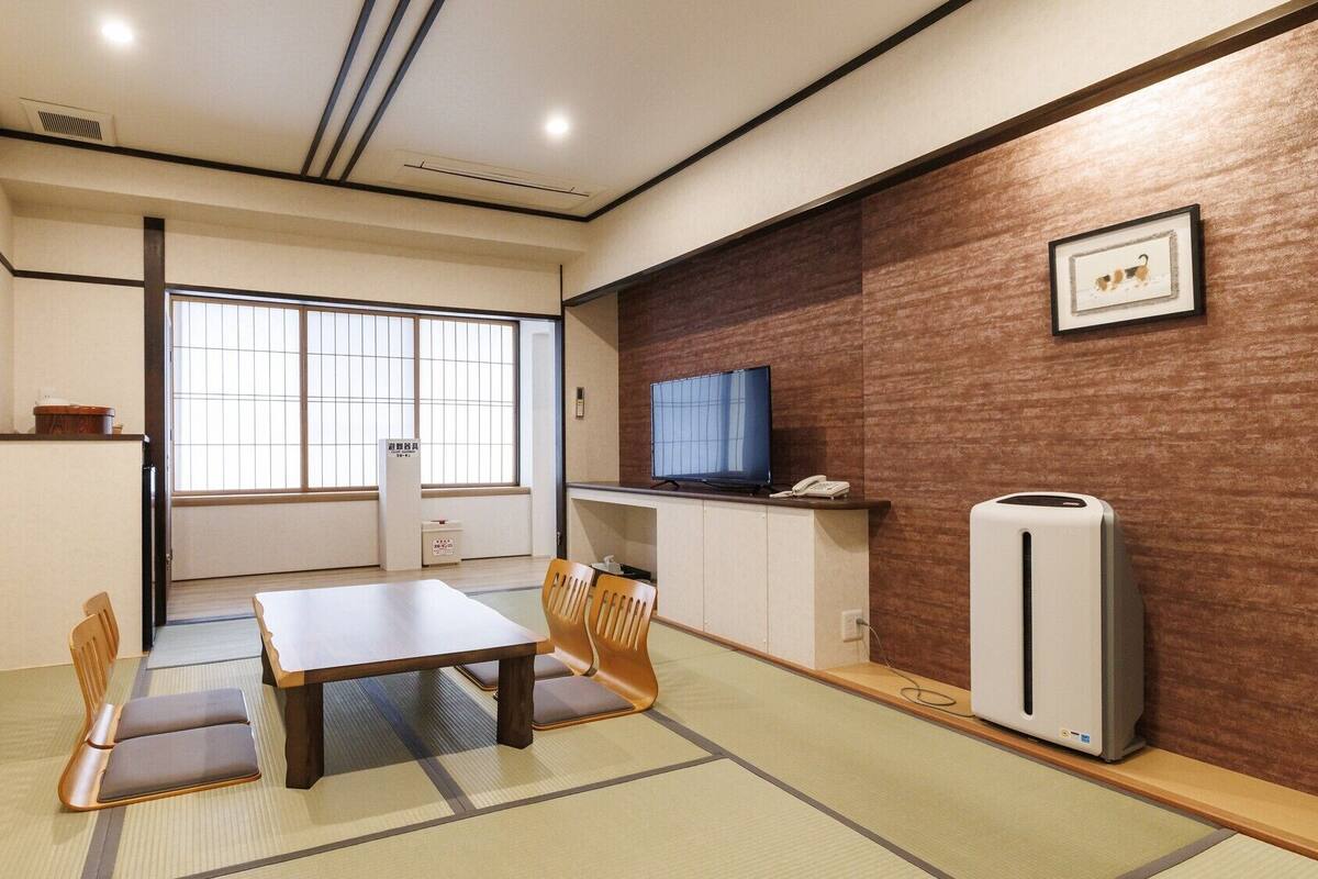 Una habitación con suelo de tatami, una mesita, sillas, televisor, refrigerador y ventana con vistas.