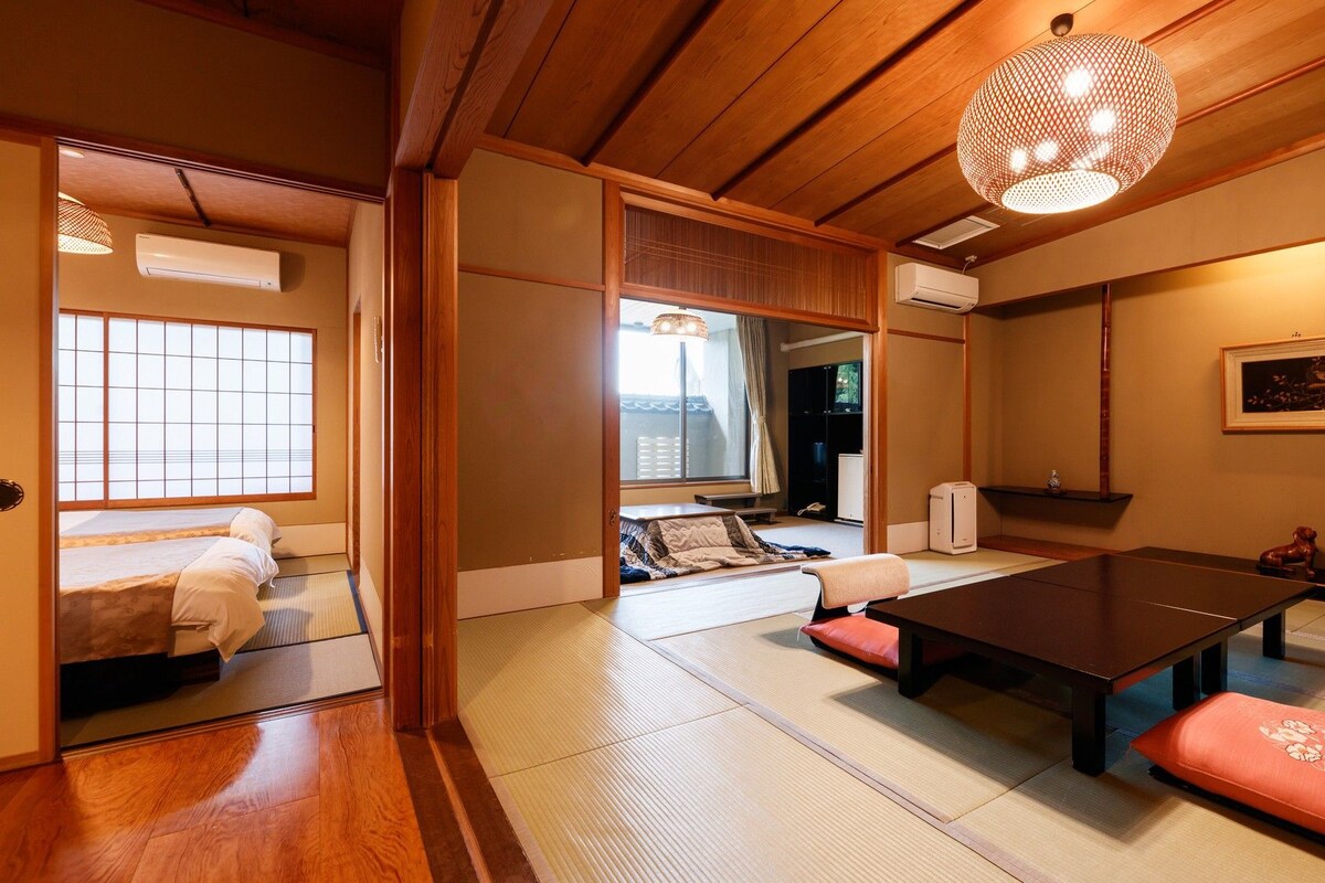 A traditional Japanese room with tatami flooring, a low table, cushions, and a hanging light fixture.