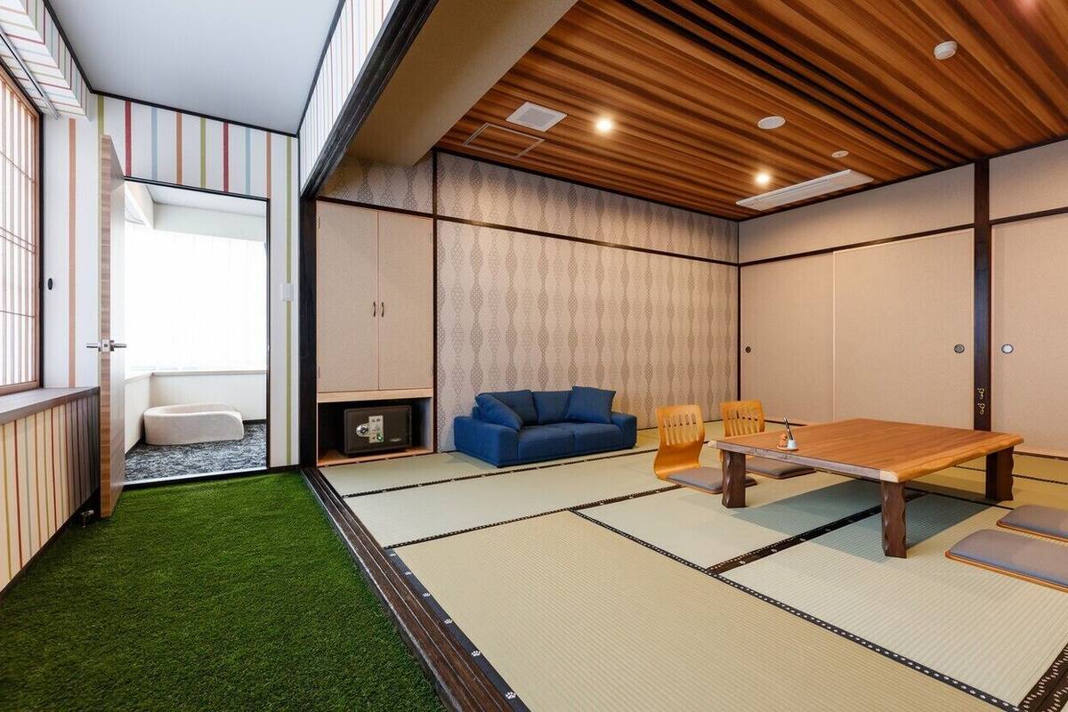 Una habitación con esteras de tatami, una mesa de madera, un sofá azul y sillas de tatami.