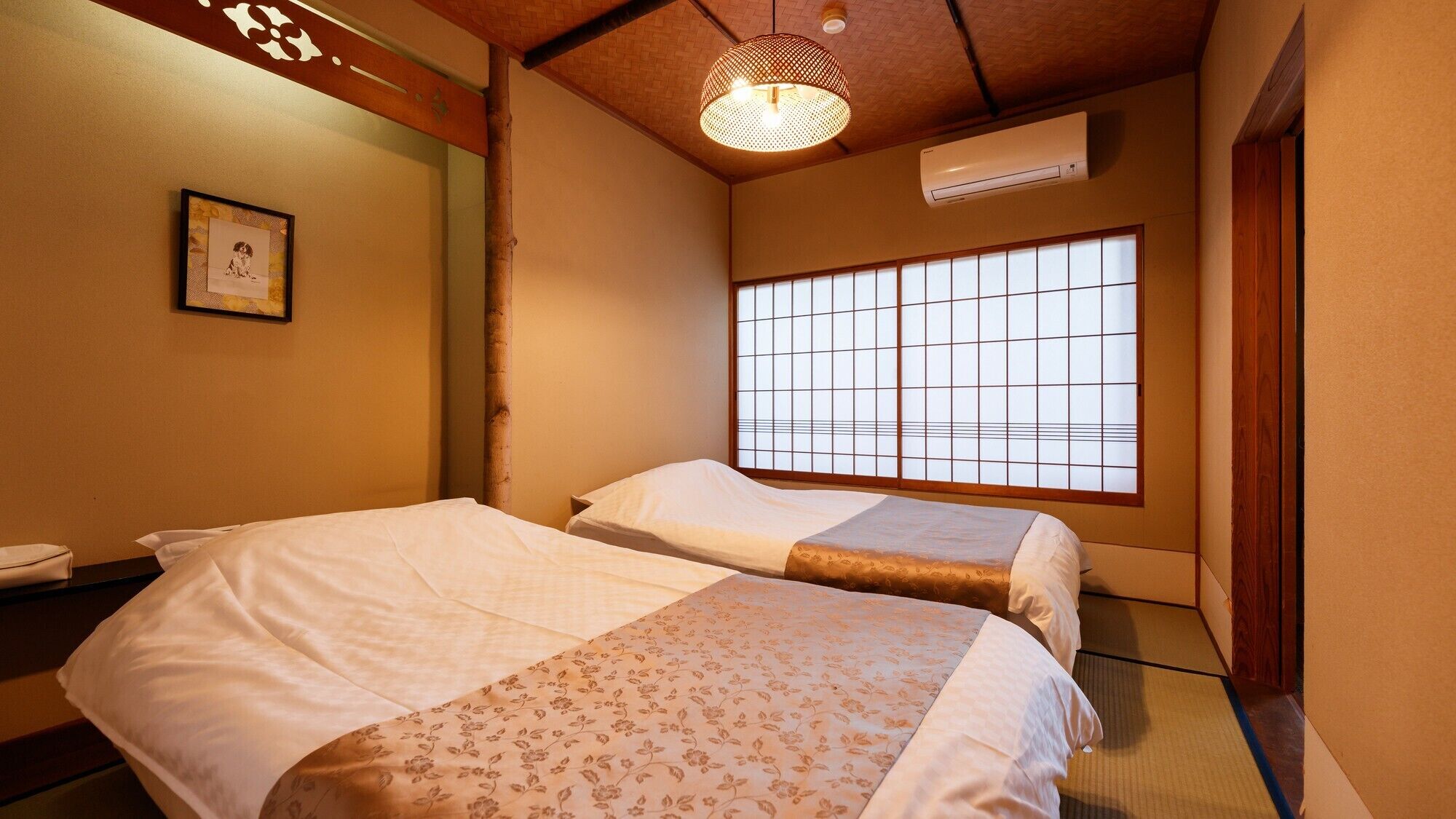 A traditional Japanese-style room with tatami flooring, two beds with floral bedding, a shoji screen window, and a hanging light fixture.