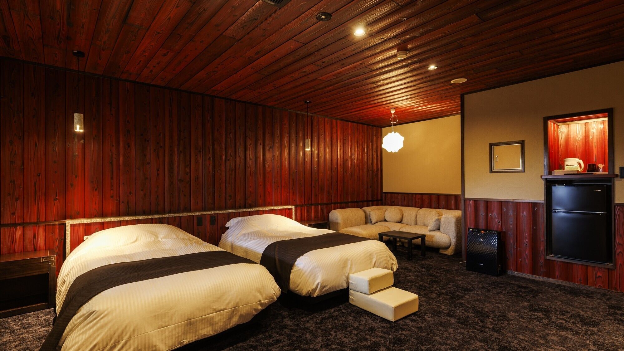 A room with two beds, a sofa, a small table, a refrigerator, and a wall-mounted TV.