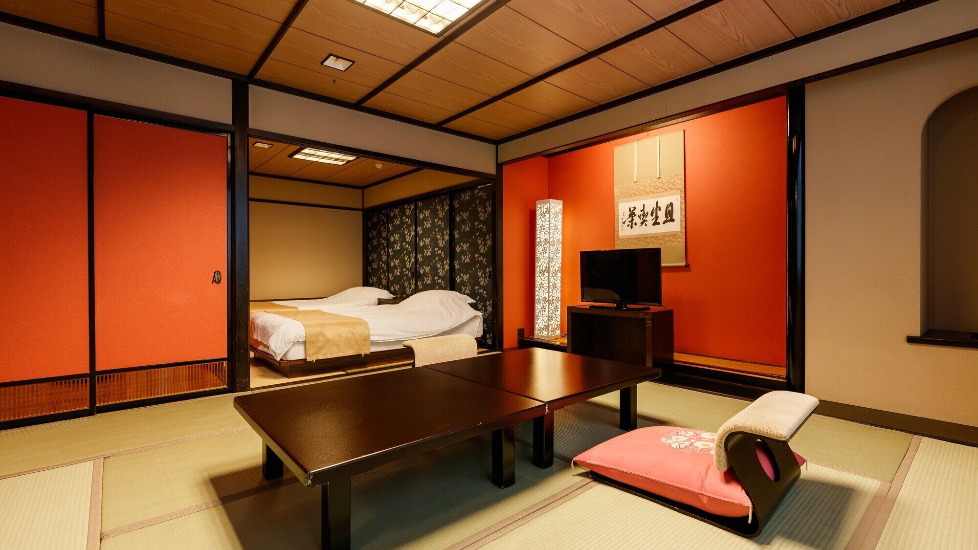 A traditional Japanese room with tatami flooring, a low table, a bed with a futon, and sliding doors.