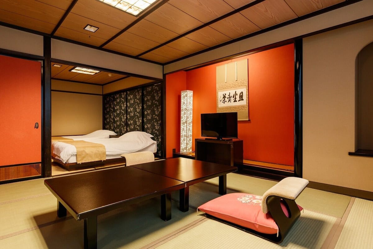 Perinteinen japanilainen huone, jossa on tatamimatto, matala pöytä, futon-patjalla varustettu sänky ja liukuvat ovet.