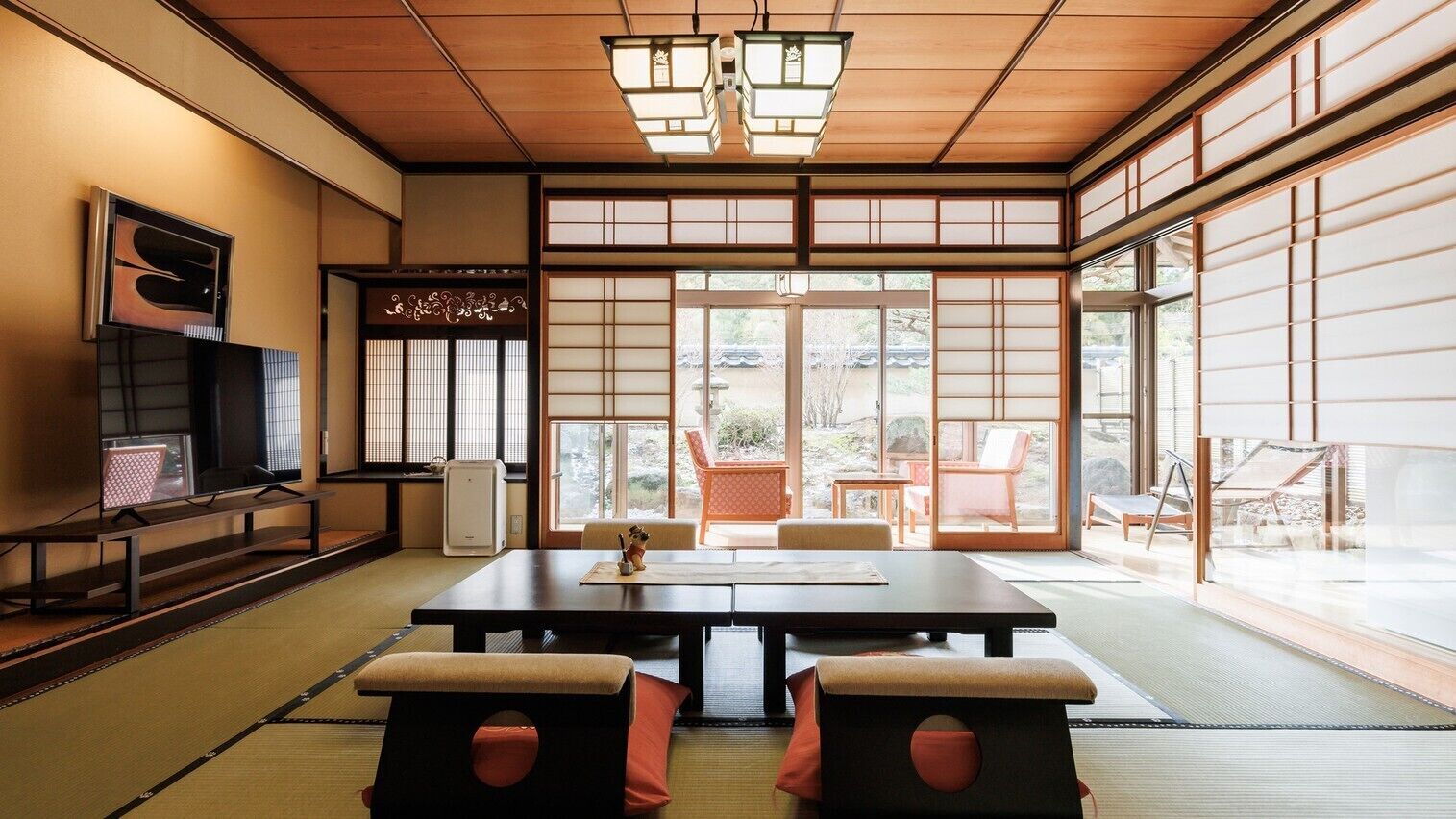 Una habitación japonesa tradicional con suelo de tatami, una mesa baja, cojines, puertas correderas y un televisor.