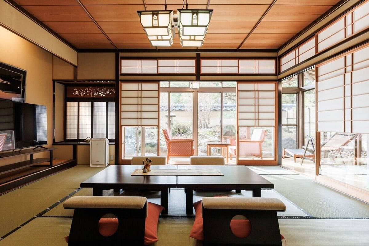 Una habitación japonesa tradicional con suelo de tatami, una mesa baja, cojines, puertas correderas y un televisor.