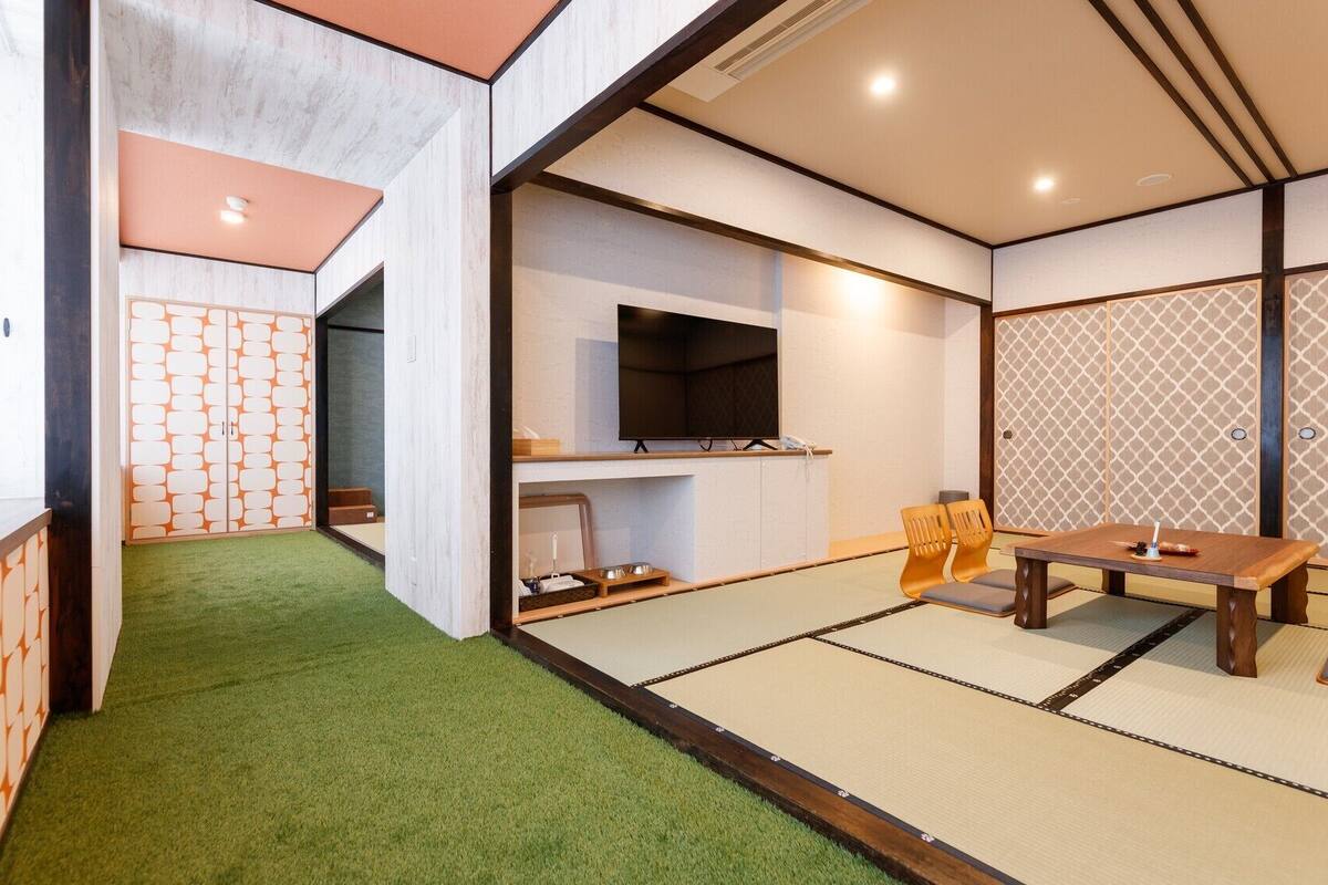Una habitación japonesa tradicional con suelo de tatami, un televisor y una mesa baja con cojines.