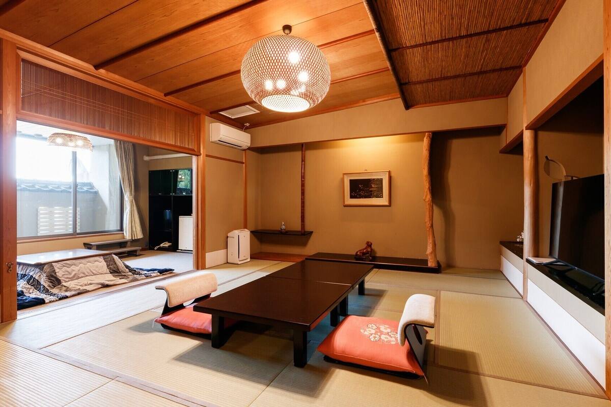 Una habitación japonesa tradicional con suelo de tatami, una mesa baja con cojines, una lámpara colgante y un televisor.