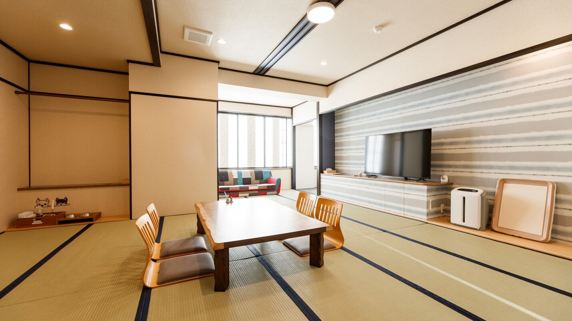 A traditional Japanese-style room with tatami flooring, a low table with cushions, a sofa, a television, and a small refrigerator.
