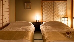 A traditional Japanese-style room with two beds, a tatami mat floor, and a sliding door. - Aiken to Sugosu Honkaku Ryokan Gekka (Awara)