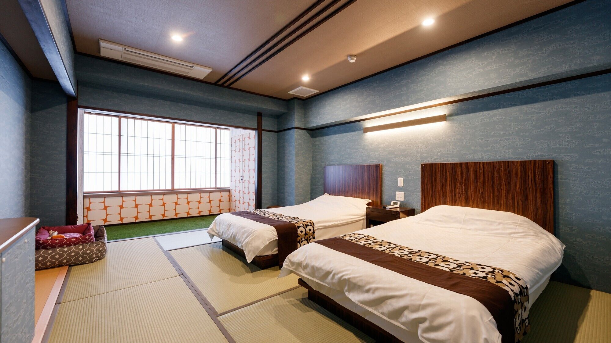 A hotel room with two beds, a futon, tatami flooring, a large window, and a ceiling with recessed lighting.