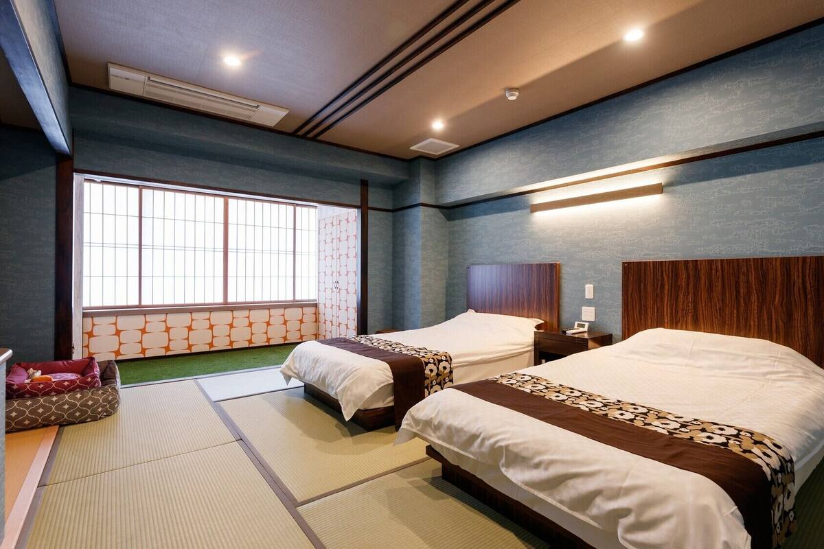 Habitación de hotel con dos camas, un futón, suelo de tatami, un ventanal grande e iluminación empotrada en el techo.