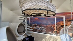 Een kamer met een hangstoel, een schommel, een spiltrap en een groot muurschildering van een canyon.