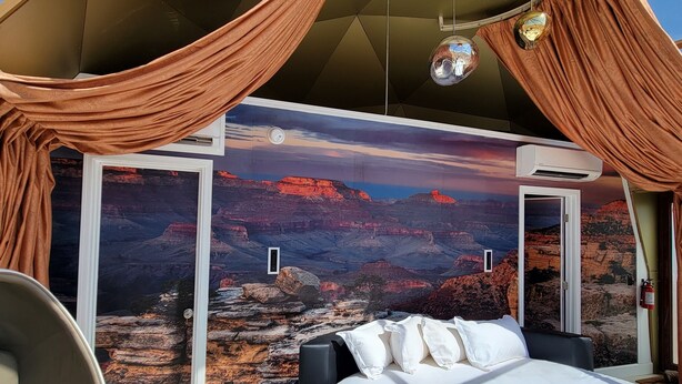 Een slaapkamer met een groot bed, een stoel, een klein tafeltje en uitzicht op een canyon door een glazen wand.