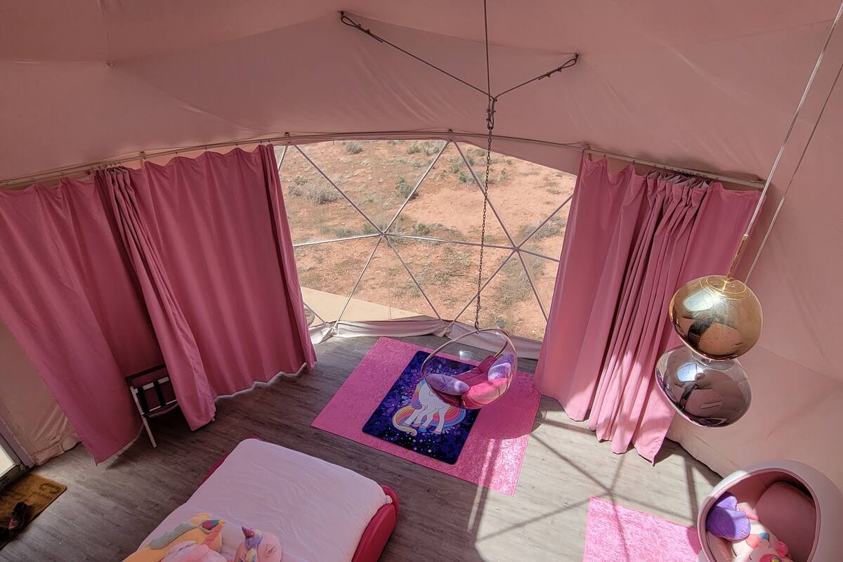 Une pièce aménagée avec une tente, un lit, des rideaux roses, un fauteuil suspendu, un petit tapis et une table ronde avec un miroir.