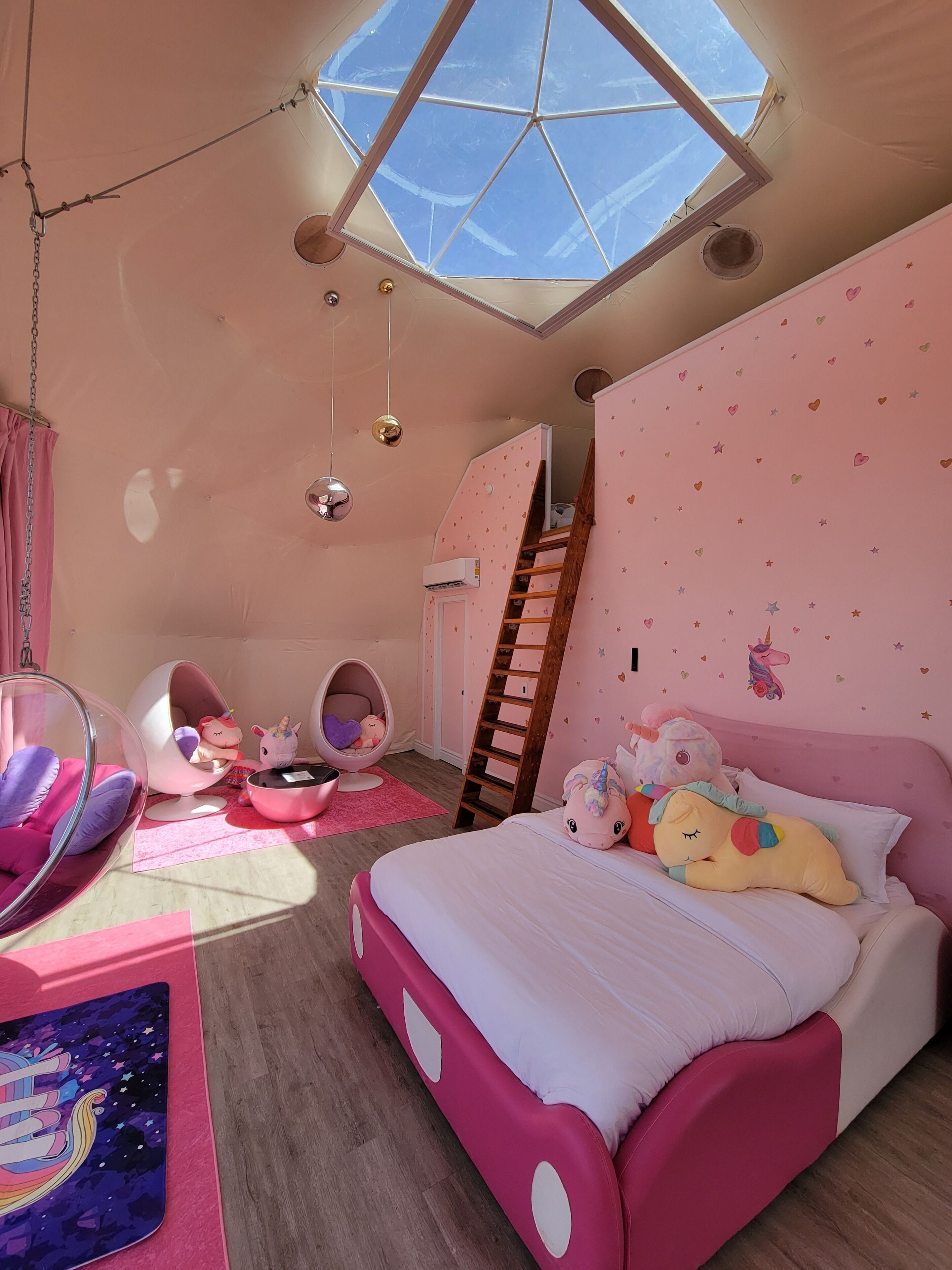 A pink-themed bedroom with a skylight, a bunk bed, a hanging chair, and a unicorn-themed bedspread.