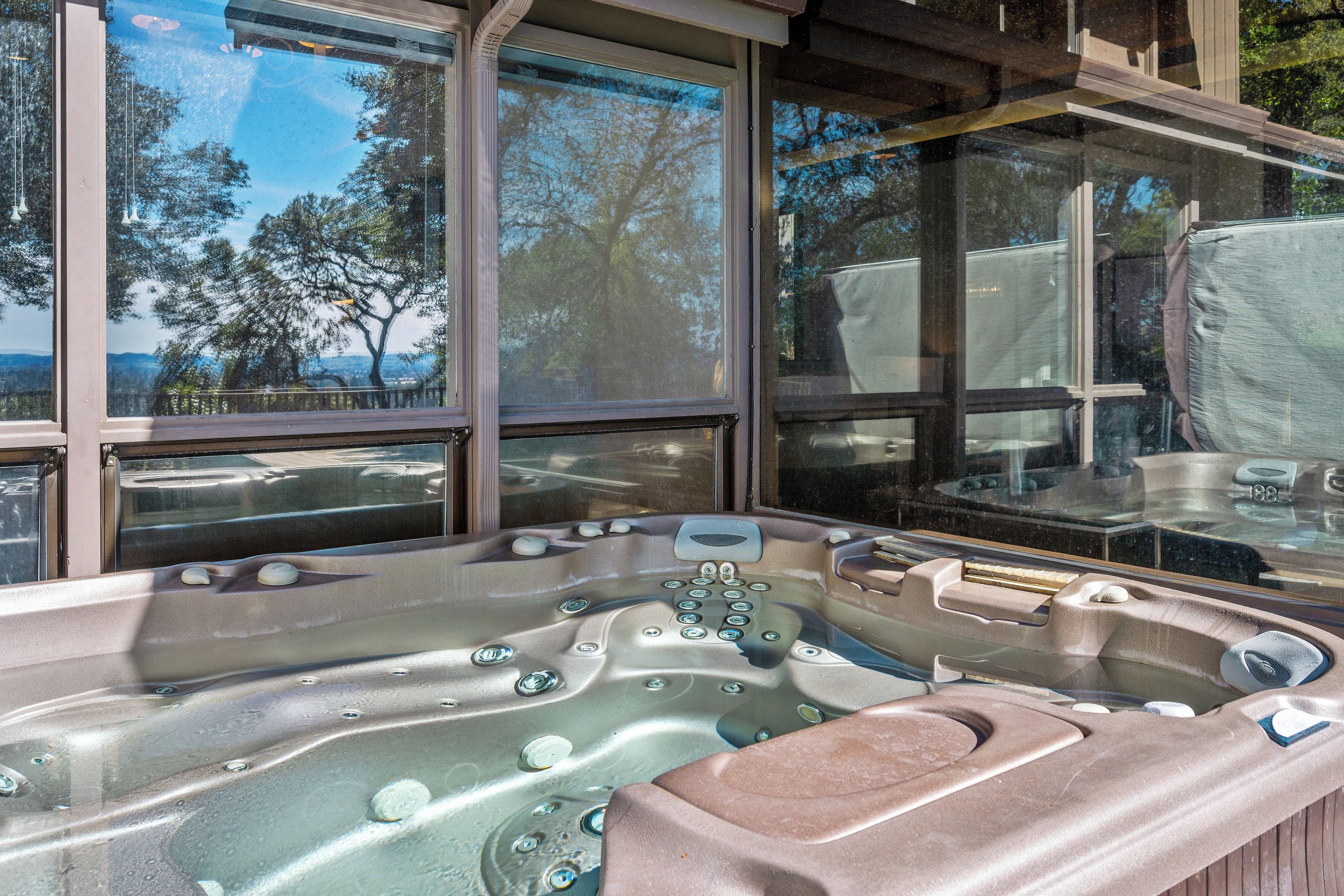 A hot tub with multiple jets, large windows, and a view of trees and mountains.
