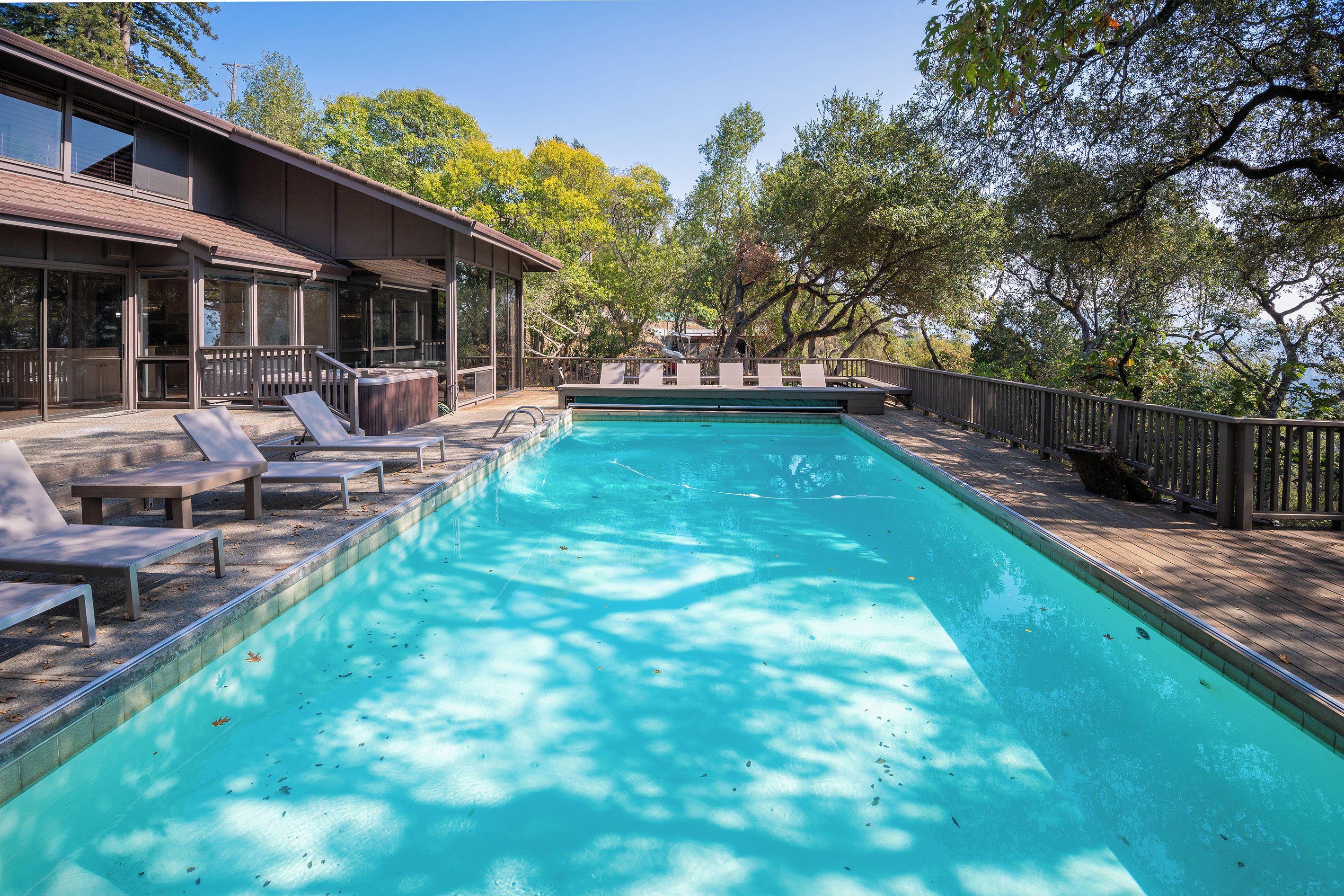 Une piscine rectangulaire à l’eau d’un bleu cristallin, entourée d’une terrasse en bois et de chaises longues.