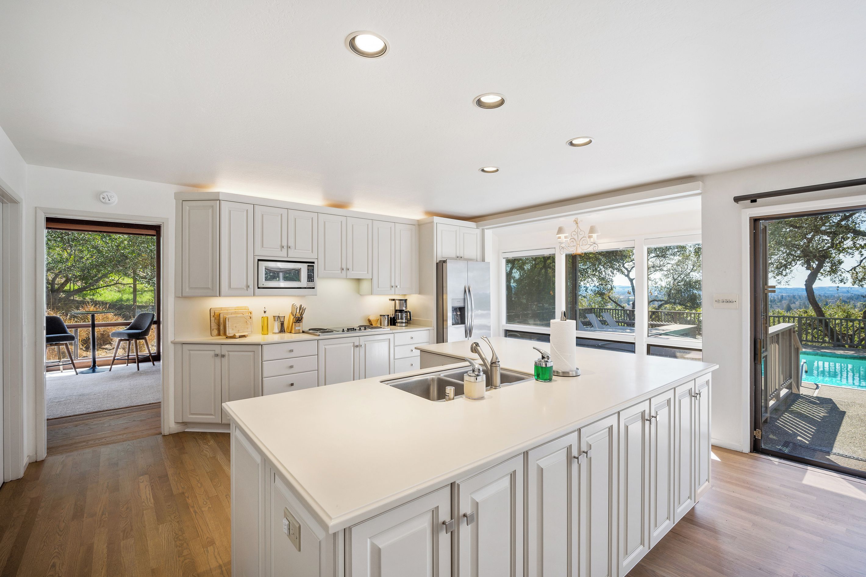 A modern kitchen with white cabinetry, a central island, and a view of a pool through large windows.