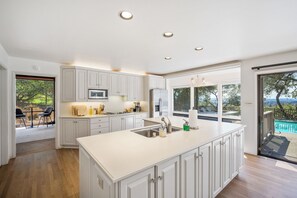 Cocina moderna con armarios blancos, una isla central y vistas a una piscina a través de amplios ventanales.