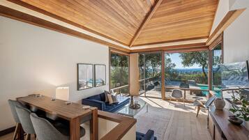 A modern interior with a wooden ceiling, a dining area, a sofa, and a view of an outdoor pool area.