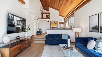 A spacious living area with a wooden ceiling, a large flat-screen TV, a blue sofa, and a coffee table.