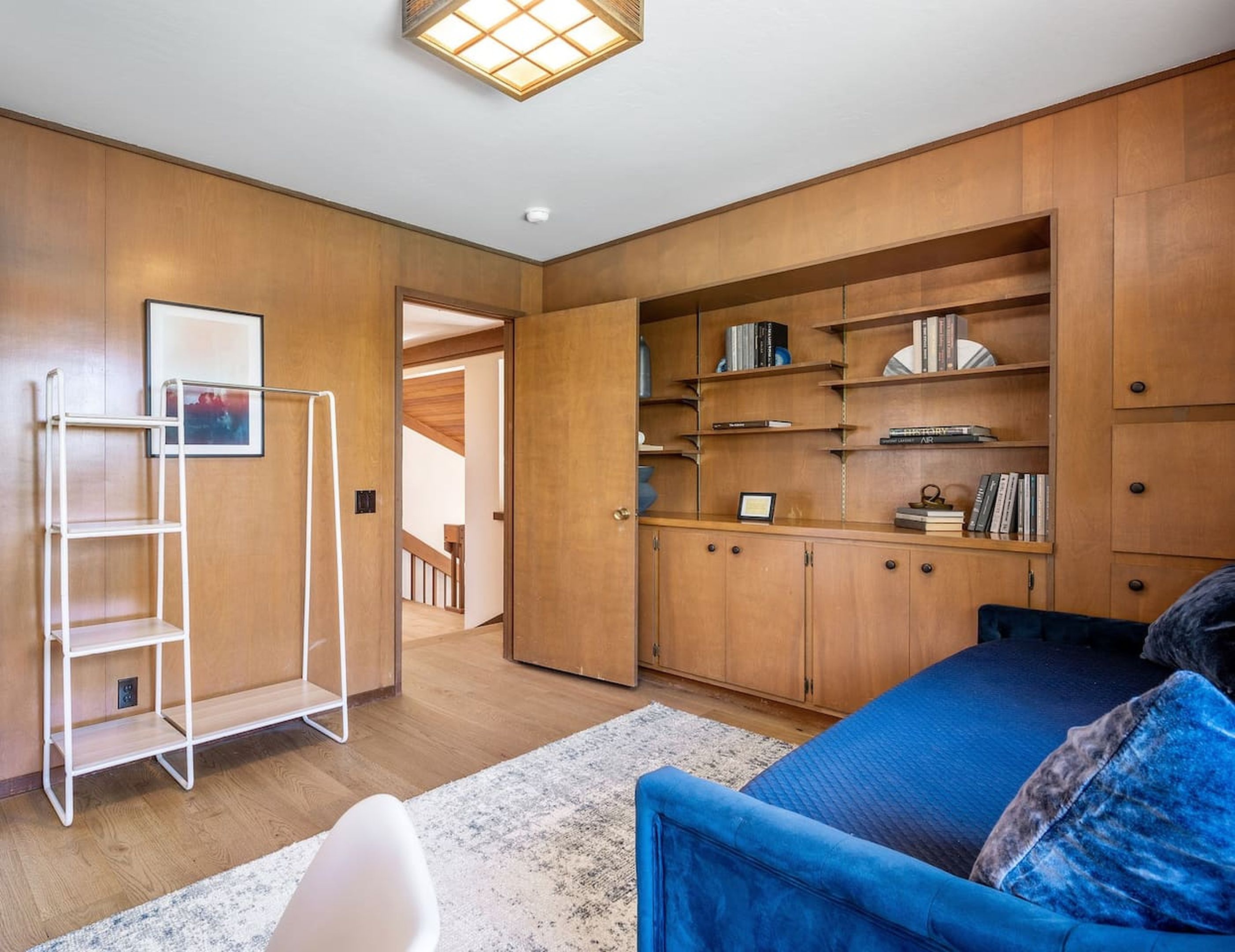 A room with a blue sofa, wooden shelving, a white ladder, and a framed picture on the wall.