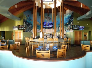 A restaurant with a central bar, multiple tables, and chairs.
